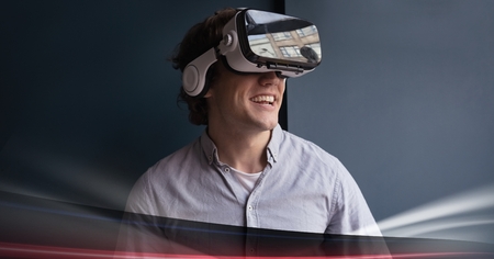 Digital composite of Man in VR headset smiling against blue background with red lightsの写真素材