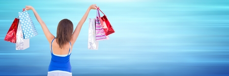 Digital composite of Back of shopper with bags in air against blurry blue backgroundの写真素材
