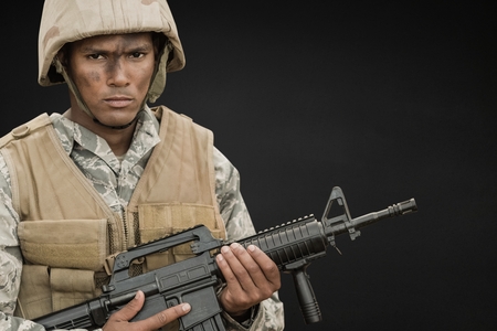 Digital composite of Angry soldier man holding a weapon against black backgroundの写真素材