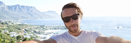 Digital composite of Millennial man taking selfie and sticking out tongue against blurry coastlineの写真素材