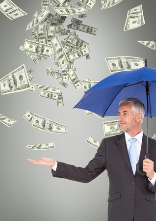Digital composite of Business man under umbrella looking at money rain against grey backgroundの写真素材