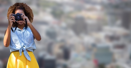 Digital composite of Millennial woman in summer clothes with camera against blurry cityの写真素材