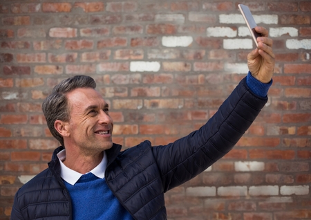 Digital composite of Man in coat taking selfie against red brick wall