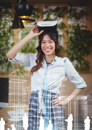 Digital composite of Happy woman with VR headset standing behind building interfacesの写真素材