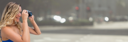 Digital composite of Millennial woman with camera against blurry streetの写真素材
