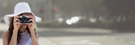 Digital composite of Millennial woman in summer hat with camera against blurry streetの写真素材