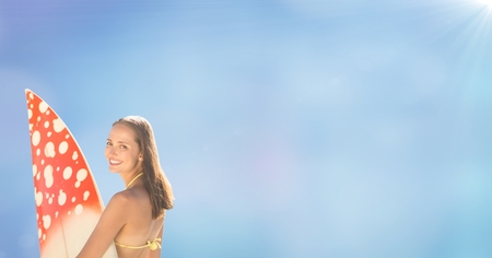 Digital composite of Back of surfer woman against blurry blue background with flareの写真素材