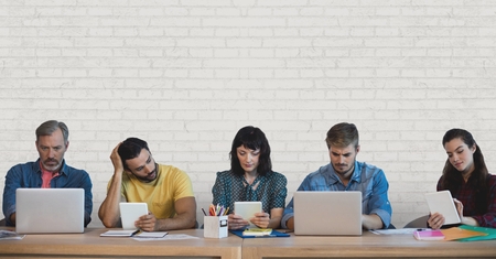 Digital composite of Business people at a desk looking at computers and tablets against white wall