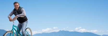 Digital composite of Middle aged man on bicycle against mountain tops and skyの写真素材