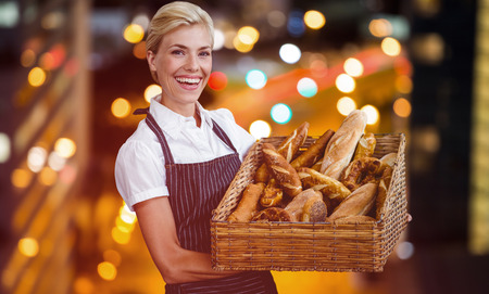 Portrait of female owner holding basket with bread against glowing road in city at nightの写真素材