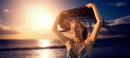 Smiling woman holding scarf in the air  against scenic view of sea against skyの写真素材