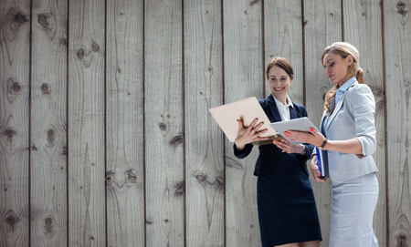 Smiling business women using digital tablet against close-up of wooden fenceの写真素材