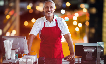 Portrait of male owner standing at counter against glowing road in city at night