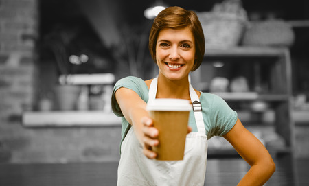 Waitress pointing away a cup of coffee against empty counter at coffee shopの写真素材