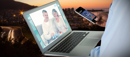 Businessman using mobile phone and laptop against view of the city by night