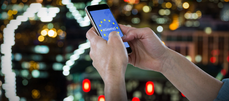 Close-up of cropped hands holding phone against defocused image of illuminated buildings in city