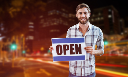 Portrait of male owner holding open sign against illuminated roads by building in cityの写真素材