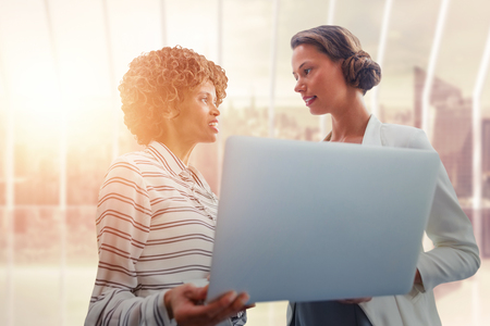 Portrait of businesswomen posing with laptop against room with large window looking on cityの写真素材