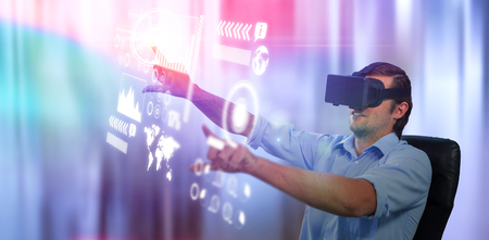 Man using virtual reality glasses while sitting by digital tablet on table against empty chairs in...