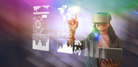 Smiling businesswoman holding digital tablet while using virtual reality glasses against view of modern meeting roomの写真素材