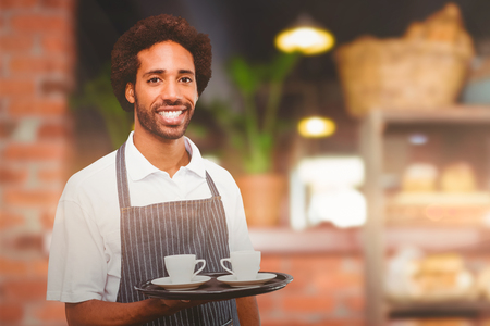 Waiter holding cup of coffee on a tray against empty counter at coffee shopの写真素材