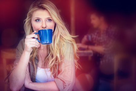 Young woman drinking coffee with man sitting in background at cafeの写真素材