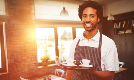 Waiter holding cup of coffee on a tray against empty chairs and tablesの写真素材