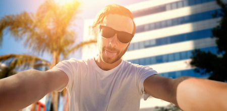 Young man taking a selfie against tree by glass buildingの写真素材