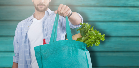 Midsection of man holding bag with vegetables against full frame shot of turquoise wallの写真素材