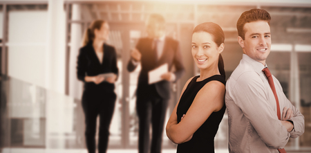 Portrait of business man and business woman posing back against back  against business colleagues interacting with each other while walking in corridorの写真素材