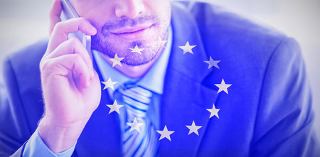 Handsome businessman sitting on sofa making a call against european flagの写真素材