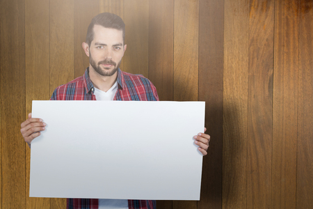 Portrait of young man holding blank placard against wooden surface with planksの写真素材