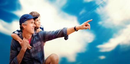 Father pointing away with his son  against blue sky with cloudsの写真素材