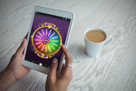 Multi colored fortune of wheel on mobile display against cropped hands of woman holding tablet at tableの写真素材