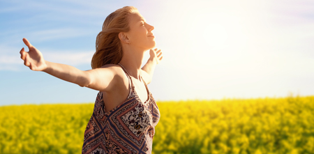 Side view of a woman raising arms up  against scenic view of yellow mustard field