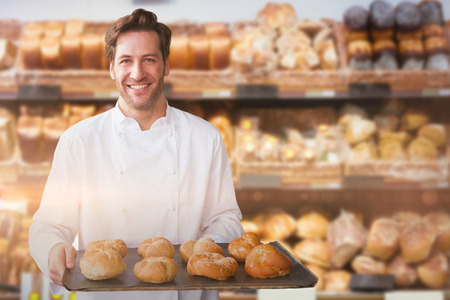 Portrait of male chef holding tray with bread against stack of breads in bakery