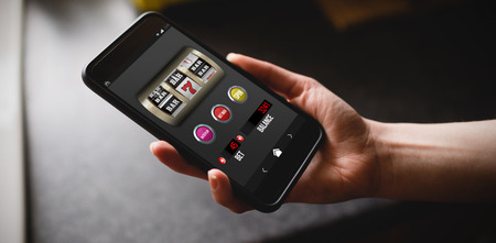 Slot machine with text and numbers on mobile display against cropped hand of woman holding phone in kitchenの写真素材