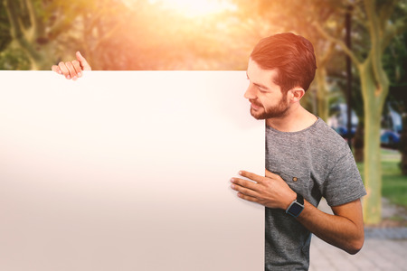 Smiling young man holding placard against white background against footpath amisdt treelinedの写真素材