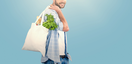 Portrait of man carrying vegetables in shopping bag against blue backgroundの写真素材