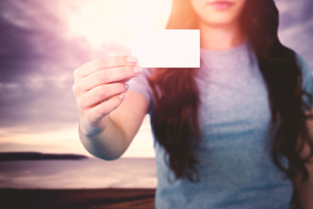 Woman holding blank card against grey sky over oceanの写真素材