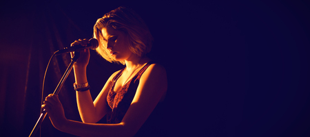 Thoughtful woman with microphone standing at nightclub