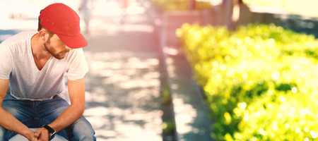 Man thinking and wearing red hat  against blur view of parkの写真素材