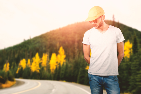Model wearing cap and sunglasses against white background against road by autumn treesの写真素材