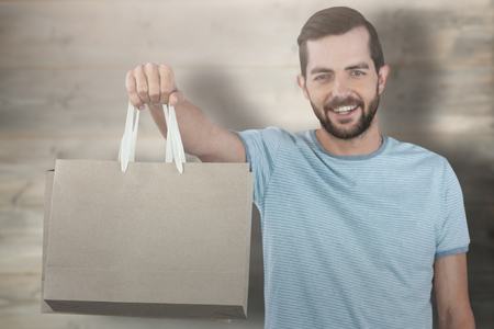 Portrait of smiling man showing shopping bag against bleached wooden planks backgroundの写真素材