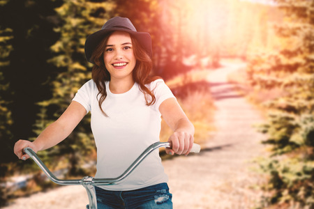 Portrait of happy woman cycling on bicycle against road through forestの写真素材