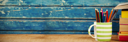 Colored pencils in cup by books on wooden tableの写真素材