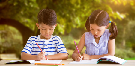 Children writing on books at table against trees and meadow in the parkの写真素材
