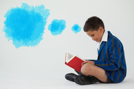Digital composite image of blue spray paint against schoolboy reading book on white backgroundの写真素材