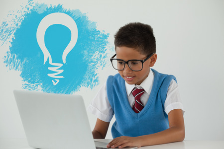 Digital composite image of light bulb on blue spray paint against schoolboy using laptopの写真素材
