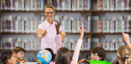 Students raising hands while teacher teaching against library shelf